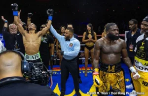 Blair Cobbs celebrates his victory with arms raised as the referee declares him the winner, while a disappointed Adrien Broner stands nearby.